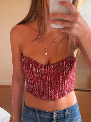 Röd tubtopp i tweed-look - Trendig röd tubtopp med bandeau-modell och snyggt rutigt mönster. Toppen är croppad och har en strukturerad tweed-känsla som ger en cool vibe. Perfekt att styla med jeans eller kjol för en chic look.