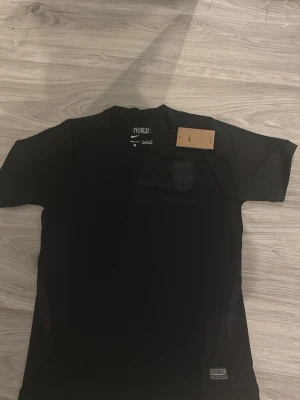 Svart Norge fotbollströja Nike - Snygg svart fotbollströja från Nike med Norge-emblem på bröstet och diskret Nike-logga. Tillverkad i lätt och ventilerande Dri-FIT-material som passar perfekt till träning eller match. Rund hals och korta ärmar för en sportig look. Storlek S, sitter som M