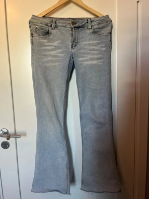 Ljusblå bootcut jeans med rå kant - ljusblå bootcut jeans med slitningar framtill och råa, avklippta benslut. Jeansen har klassisk femficksmodell, bälteshällor och knappgylf. Skulle uppskatta som en W31/L29 (M)