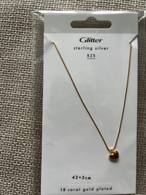 Glitter halsband med hjärthänge guld - 200kr för 1 halsband/ alla 3 för 500. Snyggt halsband från Glitter i sterling silver 925 med 18 karats guldplätering. Kedjan är tunn och elegant, och har ett litet hjärta som hänge. Längden är 42+3 cm vilket gör det lätt att justera. Perfekt accessoar för att lyfta din stil.