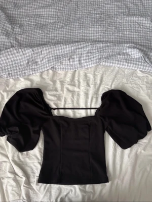 Svart topp med puffärmar - Superfin topp. Toppens form är figurnära och den har en fyrkantig halsringning. 