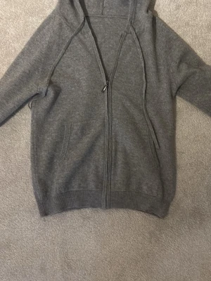 Grå zip hoodie med huva - Mysig grå hoodie med dragkedja framtill och huva med dragsko. Tillverkad i mjukt material och har ribbade muddar vid ärmslut och nederkant. Perfekt för en avslappnad stil.
