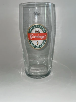 Steinlager ölglas 50cl - Säljer ett klart ölglas från Steinlager med tryckt logga i rött, vitt och grönt. Glaset rymmer 50 cl och har texten 'New Zealand Premium Lager' på framsidan. Perfekt till öl eller samling.