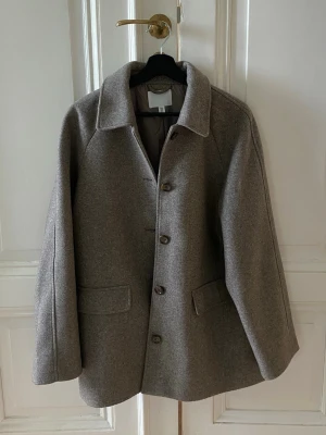 Brun coat  - Stilren brun ullrock med klassisk krage och raka ärmar. Rocken har knäppning med fyra knappar framtill och två fickor med lock. Materialet är tjockt och värmande ull, perfekt för kyliga dagar. Enkel och tidlös design som passar till mycket.