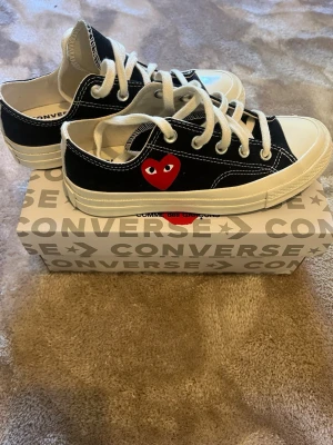 Converse x CDG Play svarta låga sneakers - Svarta Converse x Comme des Garçons Play sneakers med vitt tåparti, vita snören och sula. Ikoniskt rött hjärta med ögon på sidan. Klassisk låg modell i canvas som ger en clean och stilren vibe.