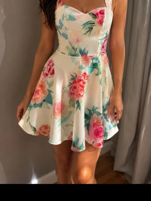 Vit blommig sommarklänning strl S  - Supersöt vit klänning med färgglatt blommönster  Klänningen har breda axelband, hjärtformad urringning och en utställd kjol som ger en lekfull look. Perfekt för varma dagar och har en fräsch, ungdomlig vibe. Ingen prislapp kvar i men helt ny och aldrig använd