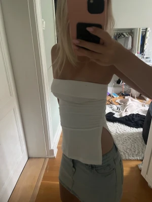 Vit axelbandslös tubtopp - Trendig vit tubtopp med bandeau-modell och slits på sidan. Toppen är axelbandslös och har en clean, minimalistisk look som passar perfekt till jeans eller kjol. Perfekt för dig som gillar stilrena plagg med en twist.