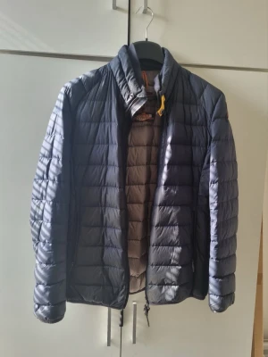 Mörkblå dunjacka från Parajumpers - Snygg mörkblå dunjacka från Parajumpers med quiltad design och hög krage. Jackan har dragkedja framtill, två sidofickor och den klassiska gula detaljen vid halsen. Perfekt för kalla vinterdagar och riktigt lätt att bära.