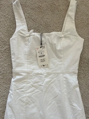 Vit ärmlös klänning från Zara - Snygg vit klänning från Zara med små rosettdetaljer framtill. Perfekt till studenten eller sommar! Nypris ca 600kr, slutsåld på hemsidan✨
