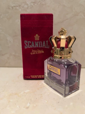 Scandal EdT från Jean Paul Gaultier - Scandal Eau de Toilette från Jean Paul Gaultier i en lyxig glasflaska med lila doft och en unik guldfärgad krona som lock. Kommer med en röd sammetsliknande förpackning med gulddetaljer. Flaskan har en fyrkantig form och tydlig etikett. Väldigt prisvärd och helt ny!!!