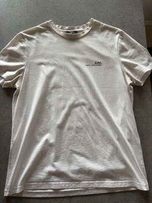 Vit t-shirt från A.P.C. - En klassisk vit T-shirt från A.P.C. Storlek S, skick 8/10. Lappen där det står storlek S har lossnat från ena sidan. Nypris ligger på ca 1200kr. Pris kan diskuteras vid snabb affär! Hör av dig vid frågor!
