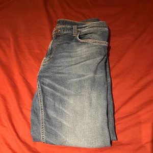 Nudie Jeans - Snygg Nudie jeans till bra pris! Byxorna är i slim fit och bra skick med snygg ljusblåa och orangea detaljer på sömmarna som är unika och ger dig en personlig stil! 