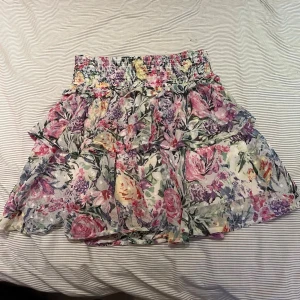 Blommig volangkjol  - Supersöt volang-kjol med blommönster i rosa, lila, grön och vit. Kjolen har resår i midjan som går att vika ner så att den blir lowwaist 🌸