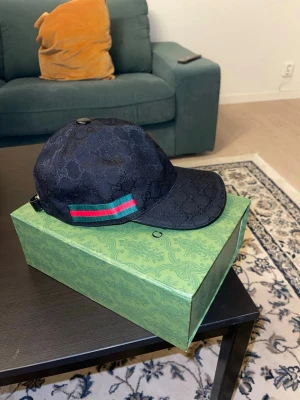 Svart keps - Snygg svart keps. På sidan finns en grön och röd randig detalj. Kepsen har böjd skärm och justerbar rem bak. Perfekt för dig som vill ha en exklusiv och trendig accessoar.