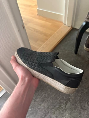 Bottega Veneta Slip Ons - Snygga svarta slip-on sneakers med flätad ovandel i läderimitation och vita. Går lätt att tvätta så dom ser nya ut igen.