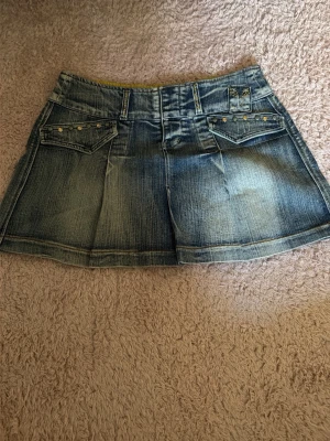 Blå jeanskjol med fickor och nitar - Säljer en blå jeanskjol, den är köpt second hand så hittar inget märke eller storlek men skulle säga ungefär m eller 36.