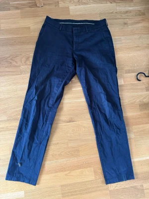 Mörkblå chinos från Tiger of Sweden - Snygga mörkblå chinos från Tiger of Sweden med klassisk rak passform och bälteshällor. Tillverkade i ett mjukt bomullsmaterial som ger en skön känsla. Perfekta för dig som vill ha en stilren och enkel look. Vet ej hur man tittar storleken men skulle gissa att de sitter som en 30/30