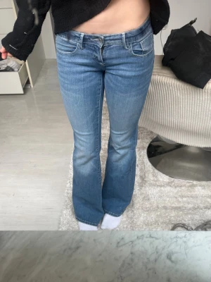 Blå bootcut jeans med låg midja - Säljer ett par ljusblå bootcut jeans med låg midja och klassiska fickor både fram och bak. Jeansen har en lätt utsvängd passform nertill och är tillverkade i mjuk denim med lite stretch för extra komfort.