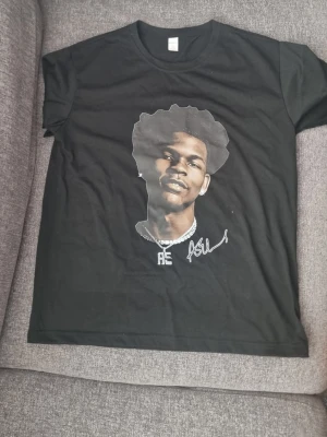 Svart t-shirt med Anthony edwards tryck - Cool svart t-shirt från Simple Fashion med ett stort tryck av en person på framsidan och vit signaturdetalj. Tillverkad i mjuk bomull och har klassisk passform med korta ärmar och rund hals. Perfekt för dig som gillar streetwear vibes. Perfekt för folk slm tränar.