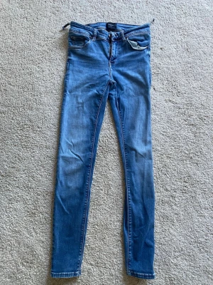 Blå skinny jeans från Vero Moda - Säljer ett par blå skinny jeans från Vero Moda med klassisk femficksdesign och dragkedjegylf. Jeansen har en smal passform och är tillverkade i stretchigt denimtyg för en bekväm känsla. Perfekta till en avslappnad och trendig look. Obs! Se sista bildens) lite skada upp vid bältet)