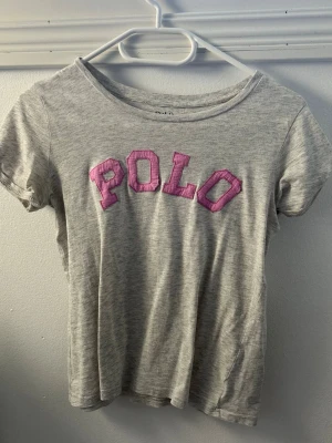Polo Ralph Lauren t-shirt - Jätte fin polo T-shirt som är grå med rosa text, Passar XS och S, bokstaven O på tröjan har sprätt upp sig lite