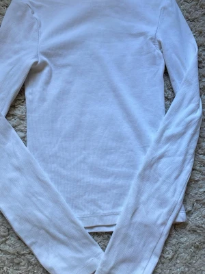 Vit ribbad långärmad topp BikBok - Klassisk vit långärmad topp från BikBok i ribbad bomull. Modellen är slim fit och har en enkel, stilren design utan synliga detaljer. Perfekt att matcha med jeans eller kjol för en clean look.
