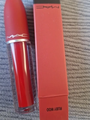 MAC Ruby Woo rött läppstift - Säljer ett MAC Ruby Woo läppstift i en ikonisk klar röd nyans. Hylsan är matt röd med silverdetaljer och transparent botten som visar färgen. Kommer i originalförpackning. Perfekt för dig som vill ha en klassisk röd läpp.
