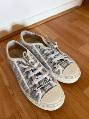 Christian Dior gråvita sneakers - Snygga sneakers från Christian Dior i grått och vitt med klassiskt Dior-mönster. Skorna har vita snören, gummisula och tydlig Dior-logga på tungan. 