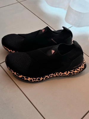 Oanvända Adidas x Parley  slip-on sneakers - Säljer ett par helt oanvända svarta slip-on sneakers från Adidas x Parley med cool leopardmönstrad sula i beige och svart. Nypris runt 2000kr storlek 40