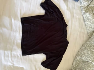 Svart tröja - En enkel svart t-shirt med korta, lösa ärmar, tight midja och rund hals. Perfekt basplagg som passar till det mesta och är lätt att styla. Tillverkad i mjukt bomullsmaterial för skön känsla hela dagen.