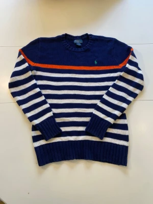 Polo by Ralph Lauren mörkblå, vit, orange tröja, storlek - Marinblå stickad tröja från Polo Ralph Lauren med vita ränder och en orange rand över bröstet. Tröjan har en grön logotyp på bröstet.  Storlek: S/M  Längd: 55 cm  Armhålsbredd: 49 cm   Ställ gärna frågor!