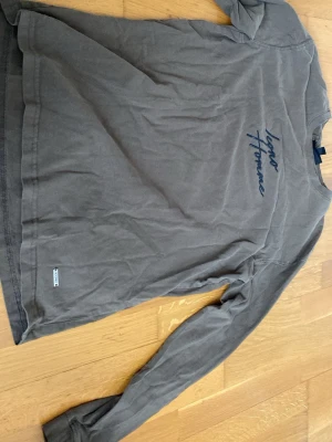 Brun långärmad topp från Icono - Snygg brun långärmad topp från Icono med diskret tryck på bröstet och liten metallbricka vid nederkanten. Tillverkad i mjuk bomull som känns skön mot huden. Perfekt till jeans eller kjol för en avslappnad look.