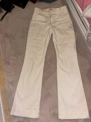 Vita bootcut jeans från Wrangler - Säljer ett par vita bootcut jeans från Wrangler med klassisk femficksdesign och broderad logga på bakfickan. Jeansen har hög midja och är tillverkade i ett mjukt bomullsmaterial. Perfekta för en clean och avslappnad look.
