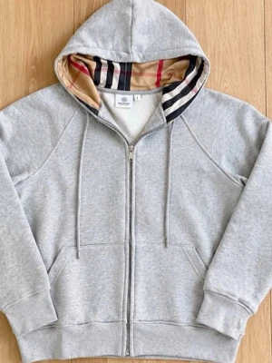 Grå zip hoodie - Snygg grå zip hoodie från Burberry med klassiskt rutigt foder i huvan. Hoodien har dragsko i huvan, två fickor framtill och ribbade muddar vid ärmar och nederkant. Perfekt för en avslappnad och stilren look.