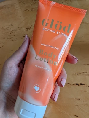 Glöd Body Lotion Peachy Mimosa - Fuktgivande body lotion från Glöd Sophie Elise i doften Peachy Mimosa. Tuben är orange med vita detaljer och har ett modernt, stilrent utseende. Produkten är vegansk och cruelty free, perfekt för dig som vill ha en återfuktande lotion med fräsch doft.