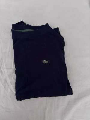 Mörkblå t-shirt från Lacoste - Snygg mörkblå t-shirt från Lacoste med den klassiska gröna krokodilloggan broderad på bröstet. Strl 176