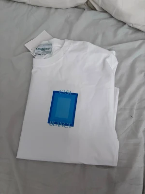 Vit Casablanca t-shirt - Säljer en clean vit t-shirt från Casablanca med ett stort blått grafiskt tryck och texten 'Casa Blanca' både fram och bak. Klassisk passform och rund hals. Perfekt för dig som gillar stilrena plagg med en twist.