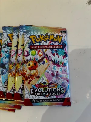 Pokémon Evolutions Prismatiques booster - Säljer flera boosterpack Pokémonkort från Scarlet & Violet Evolutions Prismatiques. Varje förpackning innehåller 10 samlarkort. Färgglad design med populära Pokémon på framsidan. Perfekt för samlare eller spelare som vill utöka sin kortsamling. 360 kort sammanlagt