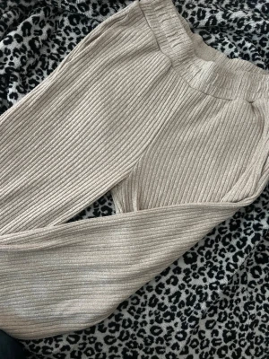 Beige ribbade loungebyxor - Mysiga loungebyxor i beige ribbat material med bred resår i midjan. Byxorna har raka ben och är perfekta för chill dagar hemma. Materialet är mjukt och stretchigt för extra komfort.