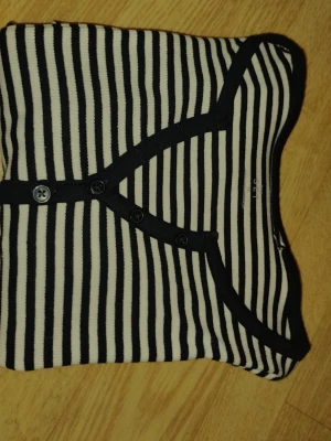 Svartvit randig långärmad Henley topp y2k Downtown  - Svartvit randig långärmad Henley topp med knappar. Från märket The set. Den kommer med 1 extra knapp. Den är gjord av 95% bomull och 5% elastan. Den är helt ny. Har aldrig använt den förutom när jag har provat den. Den är i storlek XS. Det står på deras hemsida XS (EU34). Den är gjord i Bangladesh. Jag kan sänka den om det behövs