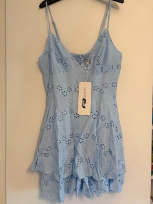 Ljusblå klänning från FB Sister - Söt ljusblå kortklänning från new yorker som köptes förra året  med broderade blommor och smala axelband. Klänningen har v-ringning och volangdetaljer nertill, perfekt för sommarens varma dagar. Tillverkad i bomull för en luftig och bekväm känsla. Det ”lagret” längst ner är shorts så det blir som ett par shorts med det övre ”lagret” som blir som en klänning. Storlek S men passar xs-s
