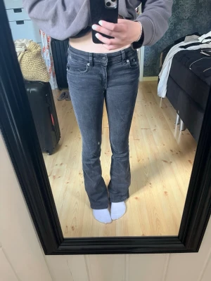 Grå bootcut jeans - Säljer ett par grå bootcut jeans med hög midja och klassiska fem fickor. Jeansen har en snygg tvätt och raka ben som går ut lite nedtill. Perfekta till vardagslooken och passar till det mesta. Stängs med dragkedja och knapp. Använd ett par gånger å blivit lite tvätt blekta men annars fult fungerande