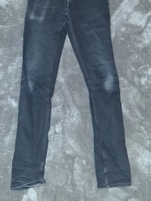 Nudie jeans - Säljer ett par svarta nudie jeans med diskreta slitningar och tvättade detaljer. Jeansen har klassisk femficksmodell och smal passform hela vägen ner. Perfekta för en avslappnad och trendig look.