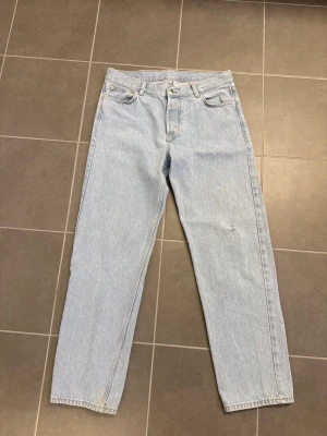 Ljusblå raka jeans från Junkyard, stl 32 - Säljer ett par ljusblå jeans med rak passform och klassisk femficksdesign. Jeansen har hög midja och är tillverkade i ett mjukt denimtyg. Perfekta för en avslappnad och trendig look.