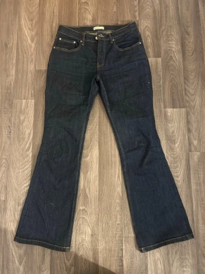 Mörkblå bootcut jeans - Säljer ett par mörkblå bootcut jeans med klassisk femficksdesign och kontrastsömmar. Jeansen har en något utsvängd passform och är tillverkade i denim. Perfekt för dig som gillar en tidlös och cool look.