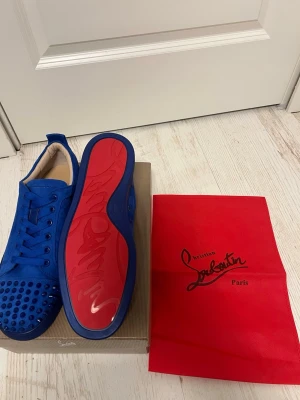 Blå Christian Louboutin  - Snygga blå sneakers från Christian Louboutin med klassisk röd sula och coola nitar på tån. Skorna är låga och har en ovandel i mocka som ger en lyxig känsla. Perfekta för dig som vill sticka ut med en unik och trendig look.