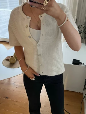 Vit kortärmad kofta  - Söt vit kofta med korta ärmar och rund halsringning. Koftan har en rak passform och knäpps med vita knappar framtill. Tillverkad i ett mjukt, ribbat material som ger en mysig känsla