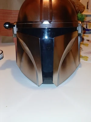 Mandalorian hjälm cosplay - Snygg Mandalorian hjälm i metallicbrons med svart visir, perfekt för cosplay eller maskerad. Hjälmen har en ikonisk design inspirerad av Star Wars och är tillverkad i plast med detaljerade former och linjer. Finns i södertälje/ gnesta