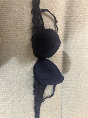 Mörkblå spets-bh från NBB Lingerie - Snygg mörkblå bh från NBB Lingerie med vadderade kupor och dekorativa spetsdetaljer längs kanterna. Bh:n har bygel och justerbara axelband för bästa passform. Perfekt för dig som vill ha både komfort och stil.