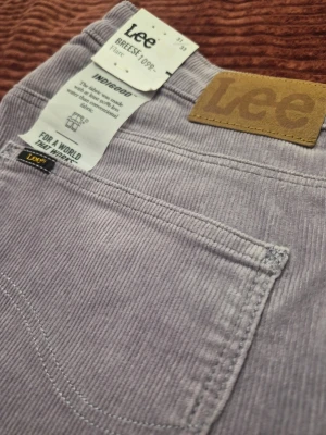 Helt nya! Vintage Lee Breese Flare high-waist corduroy lila byxor, storlek 31 33 - Säljer ett par ljuslila manchesterbyxor från Lee med klassisk femficksmodell och raka ben. Byxorna har en snygg Lee-lapp bak i midjan och är tillverkade i mjuk, ribbad manchester. Perfekta för dig som vill ha en chill och trendig look.